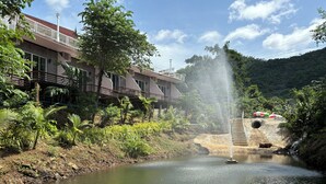 A riverside hotel with a water fountain, lush greenery, and a view of the surrounding hills. - Baan Apa Erawan Resort (Kanchanaburi)