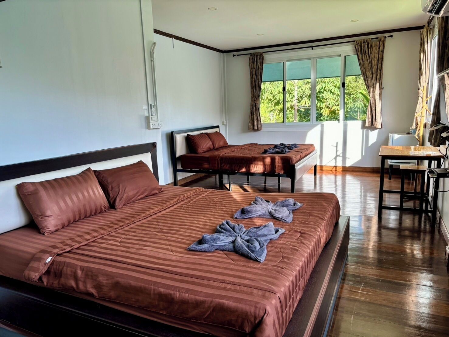A hotel room with two beds, a desk, and a window with curtains.