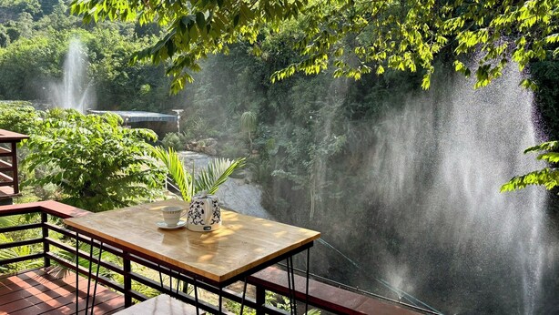 A wooden table with a potted plant and a cup, overlooking a waterfall and lush greenery. - Baan Apa Erawan Resort (Kanchanaburi)