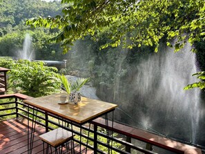 A wooden table with a potted plant and a cup, overlooking a waterfall and lush greenery. - Baan Apa Erawan Resort (Kanchanaburi)