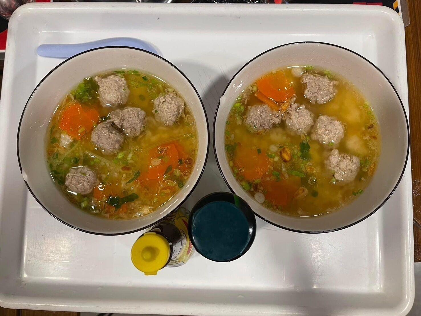 Two bowls of soup with meatballs and vegetables on a tray.