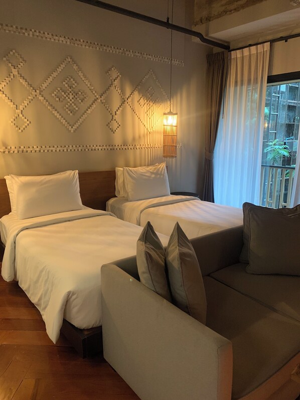 Una habitación de hotel con dos camas, un sofá, un adorno mural y una ventana con cortinas.
