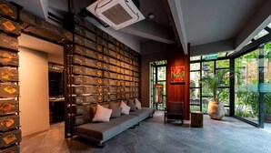 A modern interior with a wall of vintage suitcases, a sofa, and a view of greenery through large windows. - 515 VICTORY Hotel (Bangkok)