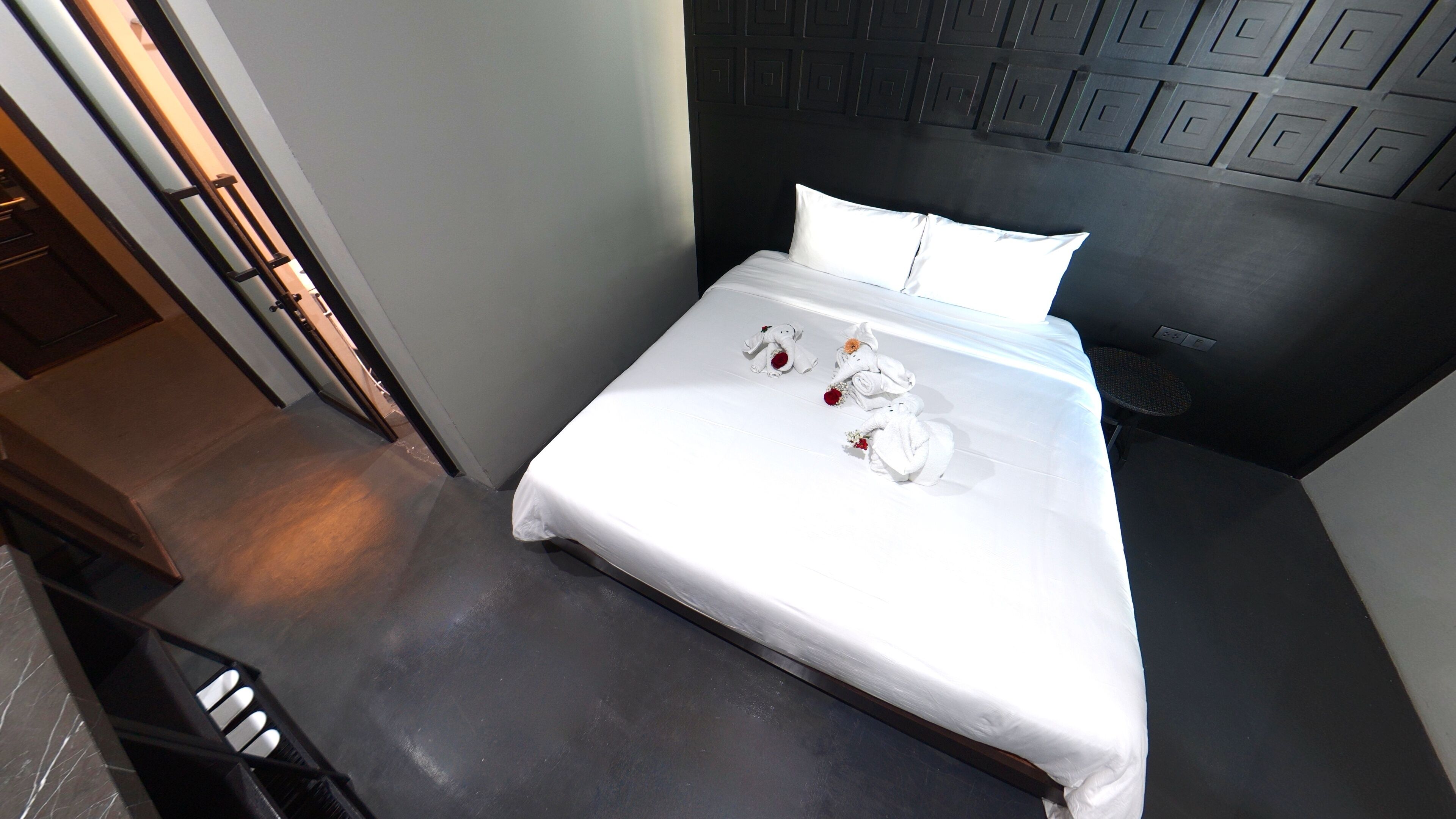 Una habitación de hotel con una cama bien hecha, un cabecero con diseño geométrico y una pequeña mesa con una silla.