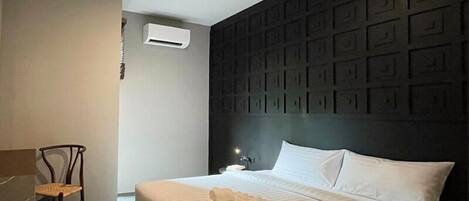 Una habitación de hotel moderna con una cama grande, una silla, una mesita de noche y un aire acondicionado instalado en la pared.