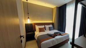 Une chambre d’hôtel avec un lit, une table de chevet, un luminaire suspendu et une vue sur l’extérieur par une fenêtre.