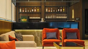 Un espace bar avec des étagères remplies de bouteilles d’alcool et de verres, un comptoir d’accueil et des sièges avec des coussins.