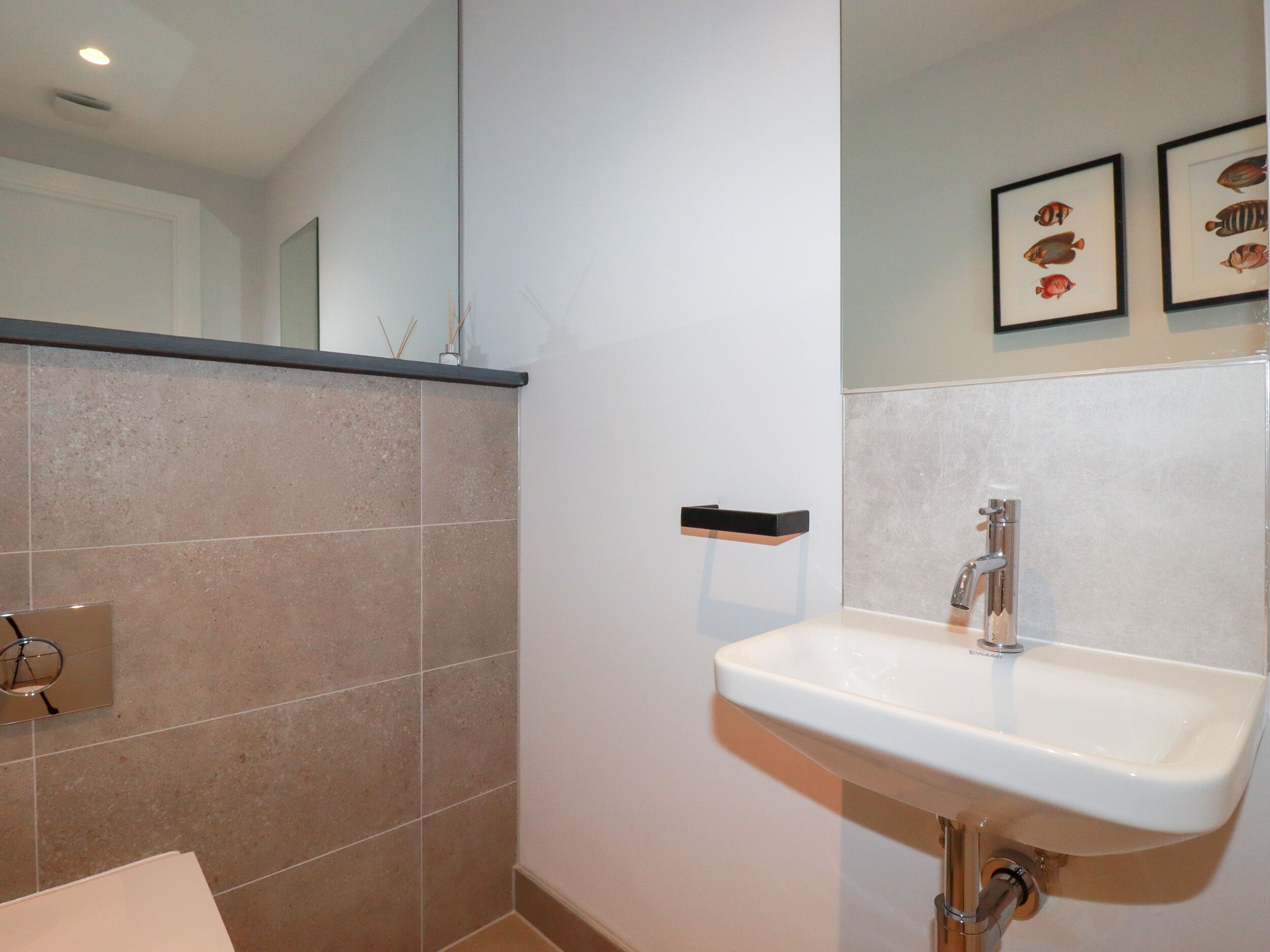 A bathroom with a white sink, a mirror, and framed fish pictures on the wall.