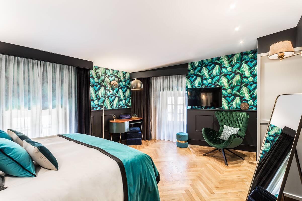 Una habitación de hotel moderna con una cama grande, un escritorio, una silla verde y un televisor.
