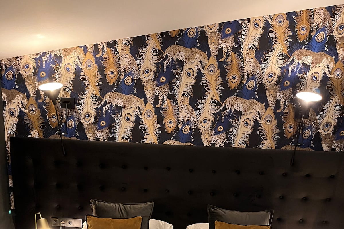Habitación de hotel con una cama grande, dos mesitas de noche con lámparas y un papel tapiz estampado.