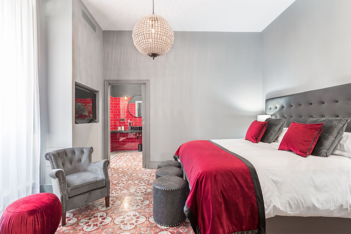 Un dormitorio moderno con una cama grande, un sillón tapizado gris y una butaca roja.
