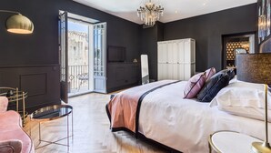 Quarto moderno com uma cama grande, um candelabro, um guarda-roupa branco e uma mesa de vidro.