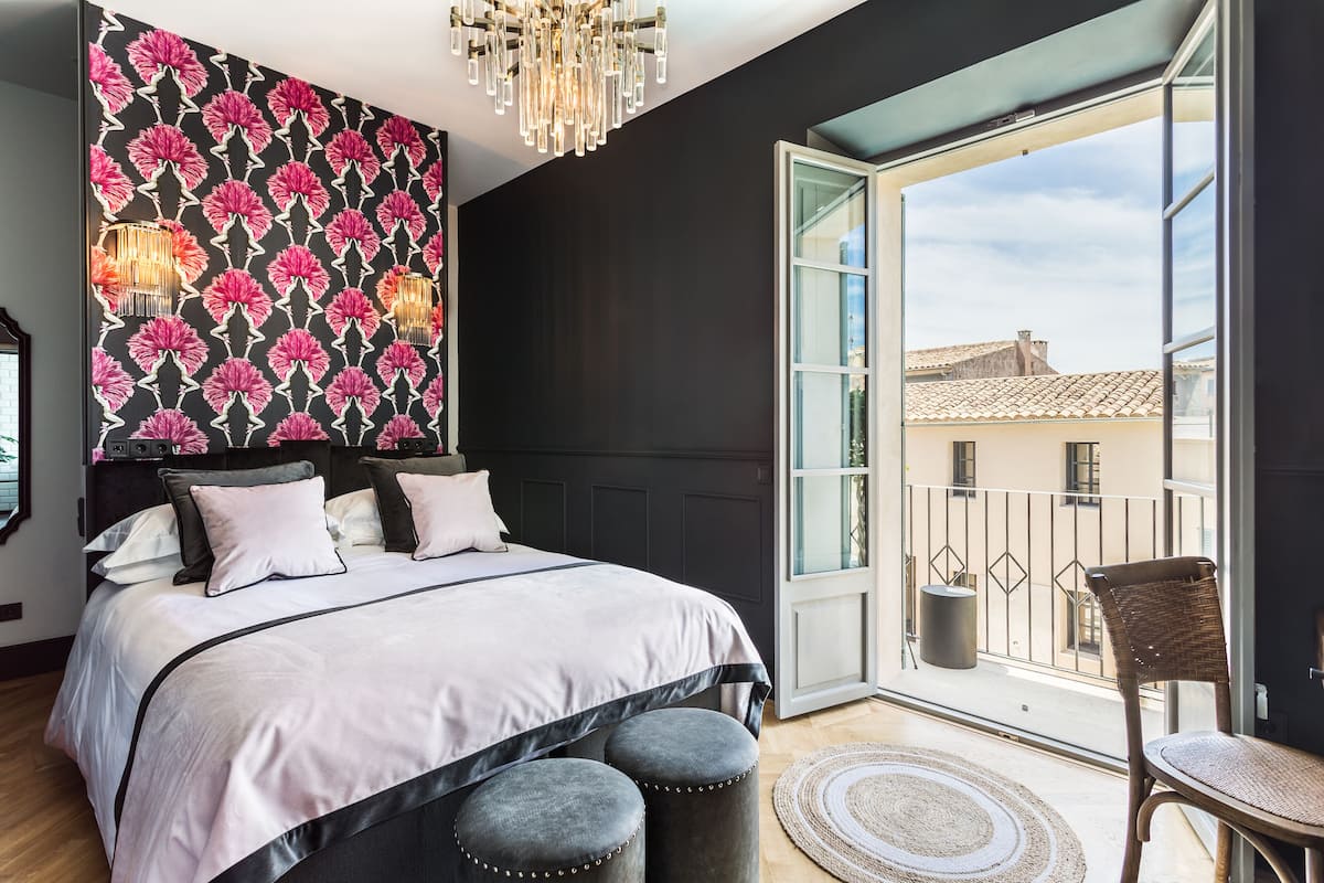 Un dormitorio con una cama grande, un balcón con una silla y vistas a edificios.