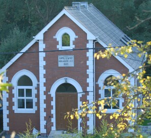 A red brick building with white trim, a central arched entrance, and a sign indicating it was built in 1930. - Capel Cartref (Swansea)