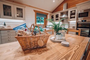 A kitchen with wooden cabinets, a dining table with a basket of bread, and a potted plant. - Merklands Wood Luxury Lodges (West Linton)
