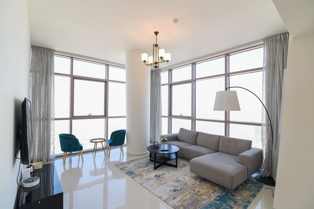 A modern living room with a sofa, two chairs, a coffee table, a TV, and large windows.