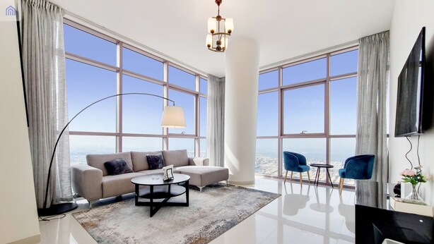 Una sala de estar moderna con un sofá, una mesa de centro y sillas, ventanas amplias con vista a la ciudad y un televisor de pantalla plana.