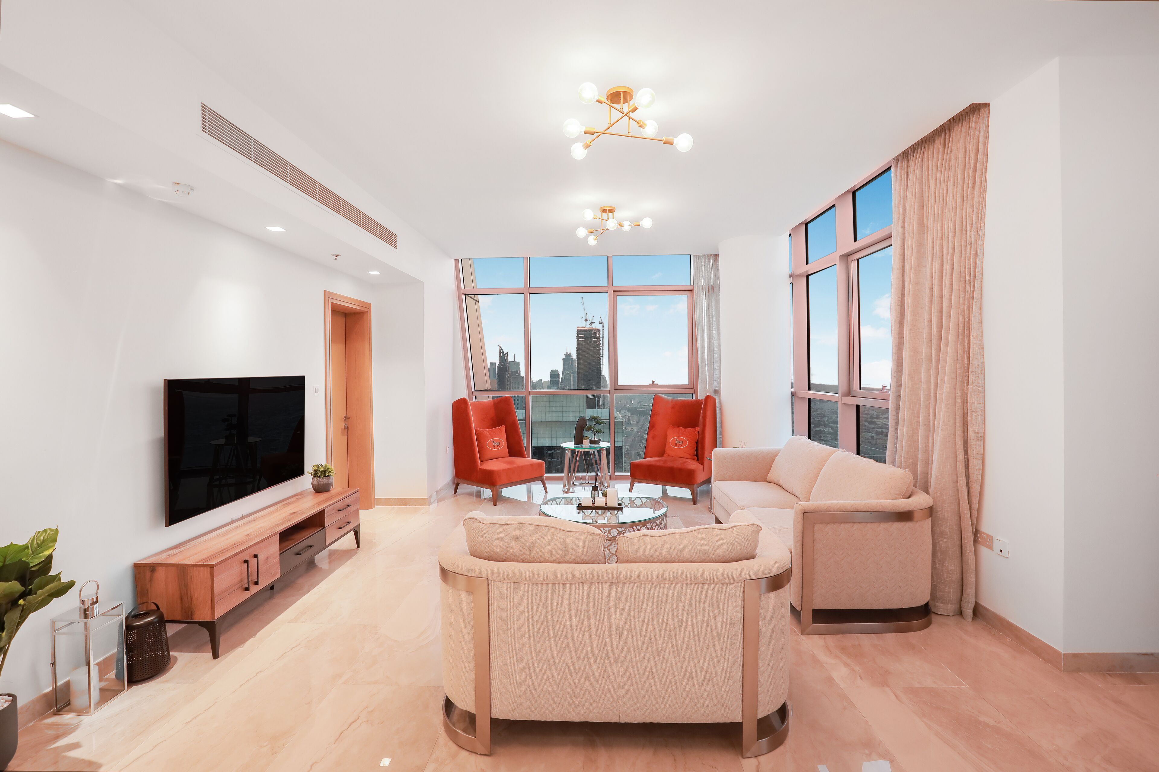 A modern living room with a flat-screen TV, two red armchairs, a beige sofa, and a coffee table.