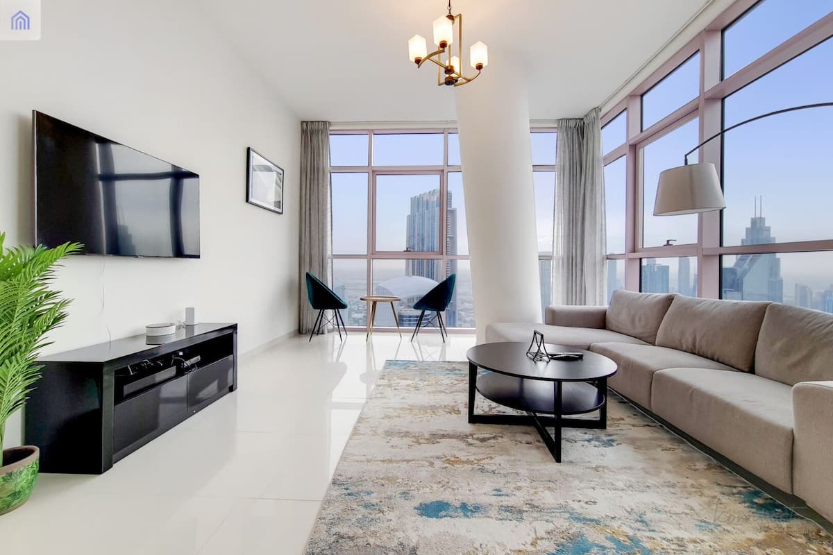 A modern living room with a flat-screen TV, a sofa, a coffee table, and a dining area with chairs.