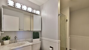 Ein Badezimmer mit weißem Waschbecken, Spiegel, Toilette und einer Duschkabine.