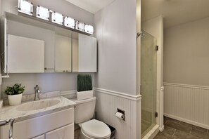 Een badkamer met een wit wastafelmeubel, spiegel, toilet en een douchecabine met glazen wanden.