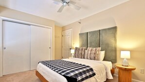 Ein Schlafzimmer mit einem Bett, einem Deckenventilator, einem Nachttisch mit Lampe und einer Tür.