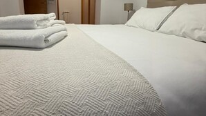 A neatly made bed with white linens and a textured blanket, a bedside lamp, and a door in the background.