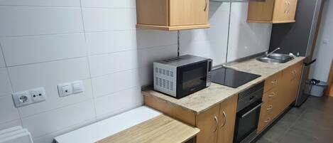 Une cuisine compacte avec des carreaux blancs, des armoires en bois, un four à micro-ondes, une cuisinière et un évier.