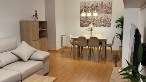 A modern living room with a sofa, a coffee table, and a dining area with a table and chairs. There is a painting on the wall and a plant on the side.