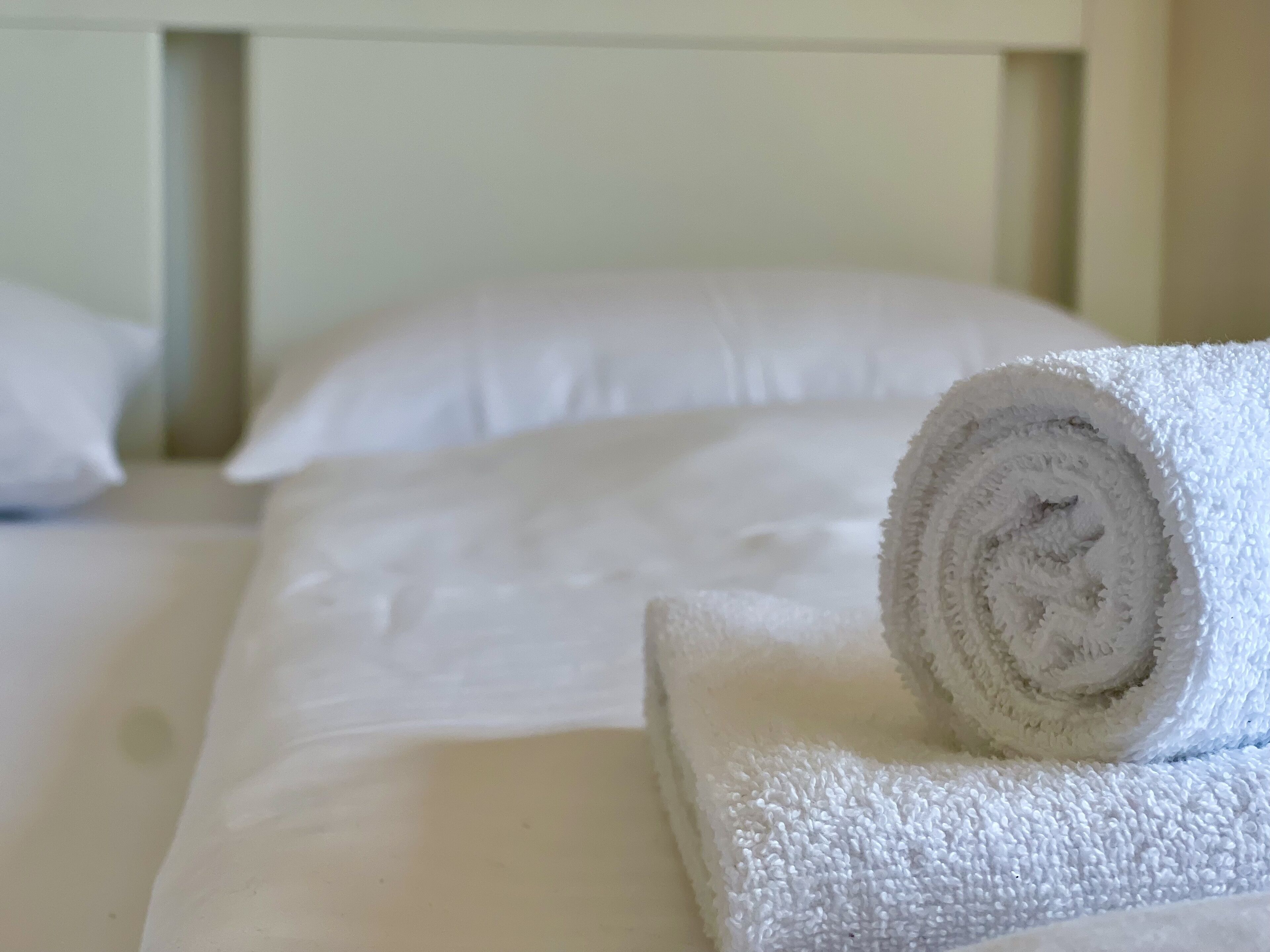 Een net opgemaakt bed met witte lakens en een opgerolde handdoek op het nachtkastje.