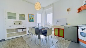 A modern kitchen with white cabinetry, a dining table set for four, and a large window providing natural light. - Apartment Reful (Kraljevica)