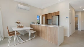 Cozinha moderna com bancada branca, armários de madeira e geladeira embutida.