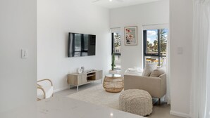 Uma sala de estar moderna com televisão de tela plana, um sofá, uma mesa de jantar e um ventilador de teto.