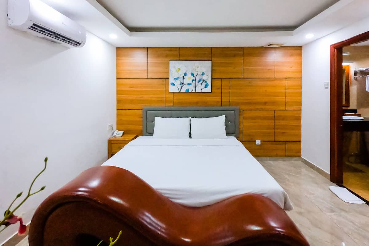 Quarto de hotel com parede de painel de madeira, cama com roupa de cama branca, telefone de apoio e unidade de ar condicionado.