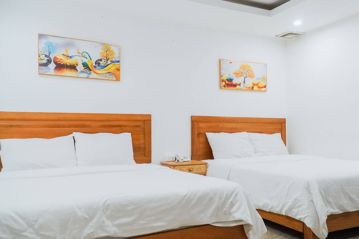Quarto de hotel com duas camas de madeira, roupa de cama branca e duas pinturas nas paredes.