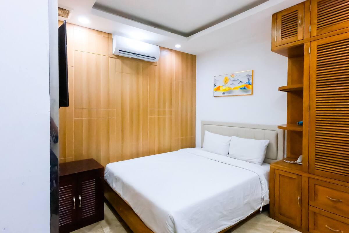Quarto com cama, guarda-roupa de madeira e ar condicionado.