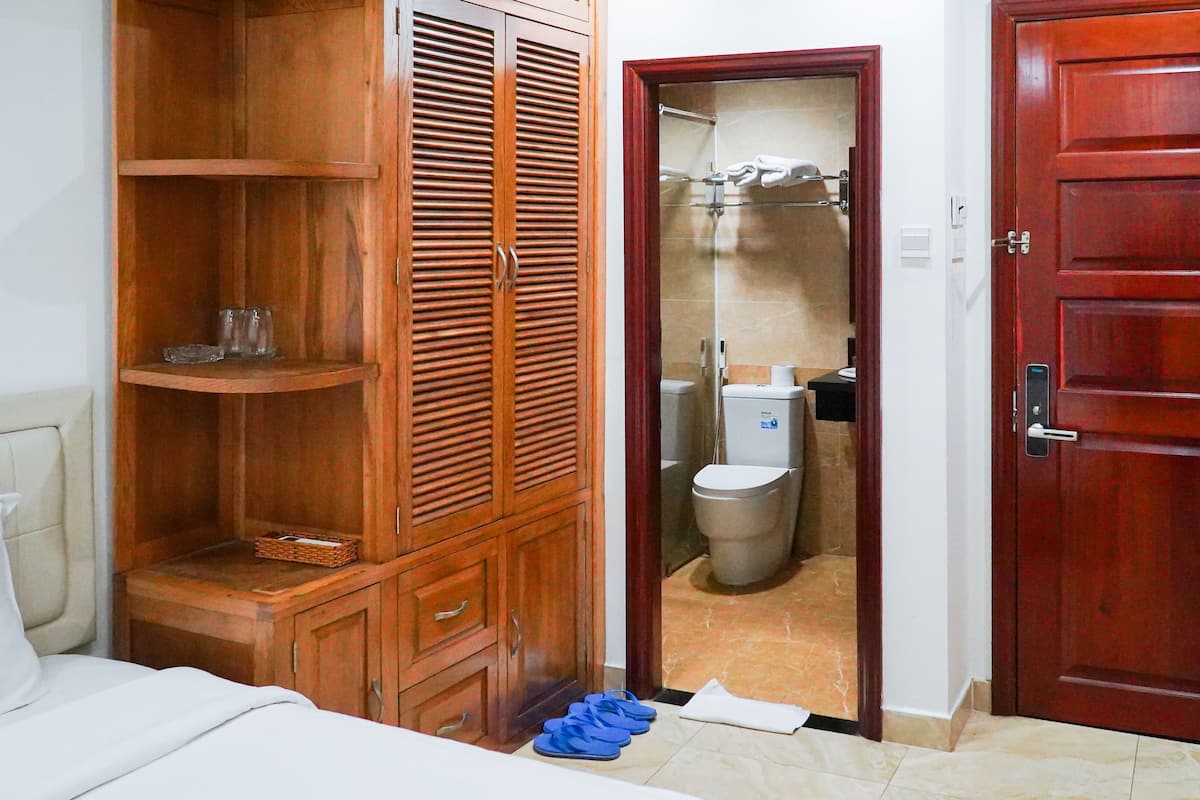 Quarto com guarda-roupa de madeira, uma cama e banheiro visível através de uma porta aberta.