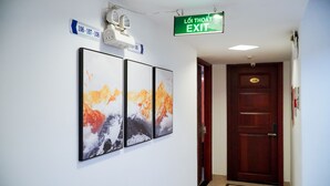 Ein Flur mit drei gerahmten Berglandschaftsbildern, einem an der Decke befestigten Projektor und einem Hinweisschild für den Ausgang.