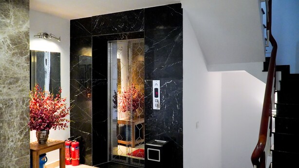 Ein modernes Badezimmer mit einem schwarzen Marmor-Waschtisch, einem Spiegel, einer roten Blumenvase und zwei Feuerlöschern auf einem Holzboden.