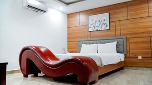 Ein modernes Schlafzimmer mit einem gewölbten roten Sessel, einem grau gepolsterten Bett und einer Holzpaneelwand mit einem Blumenbild.