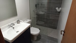 Et moderne badeværelse med bruseafskærmning i glas, en hvid vask og et toilet.