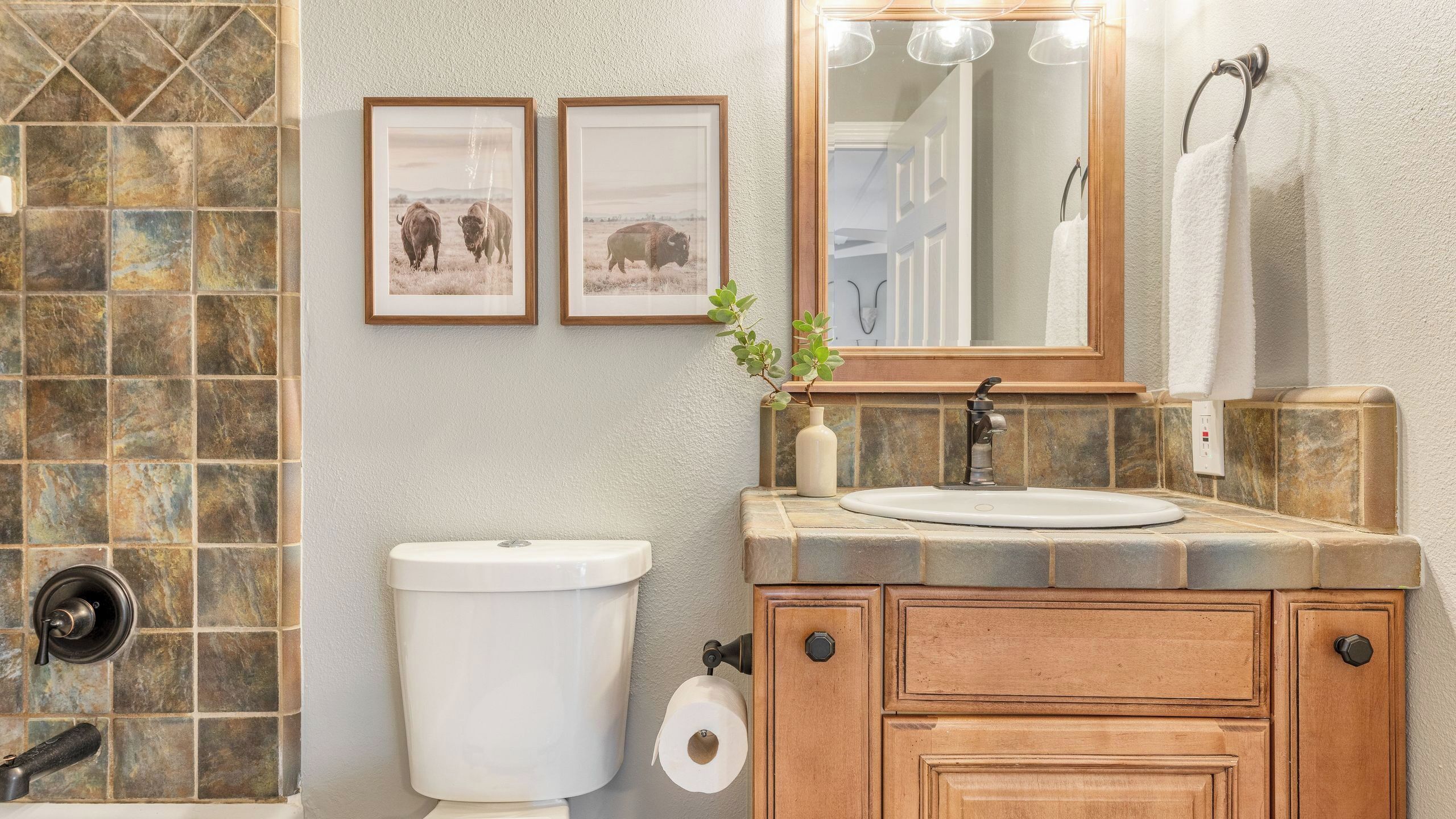 A bathroom with a toilet, sink, vanity, and framed pictures on the wall.