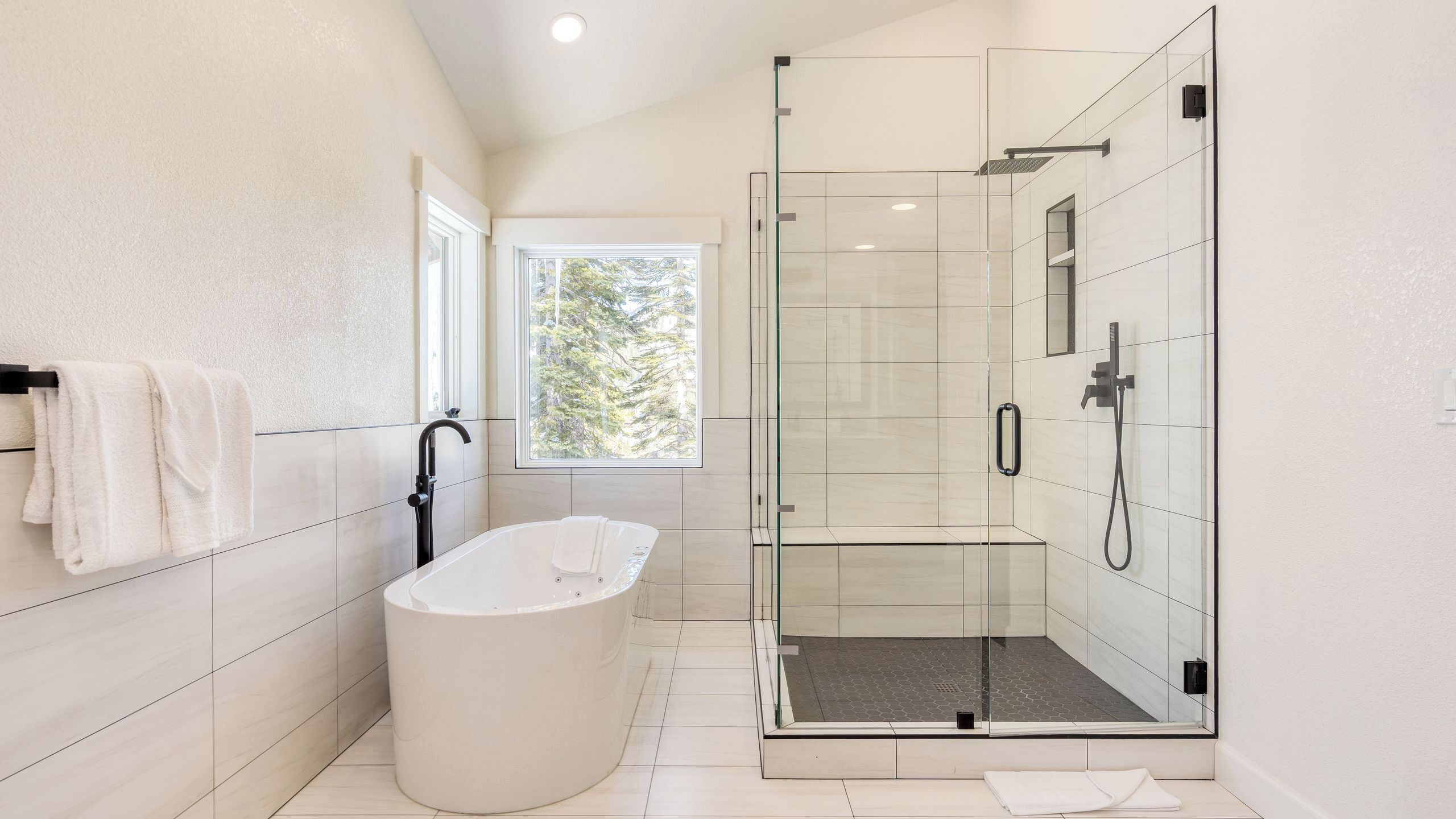 A modern bathroom with a freestanding bathtub, a glass-enclosed shower, and a window providing natural light.
