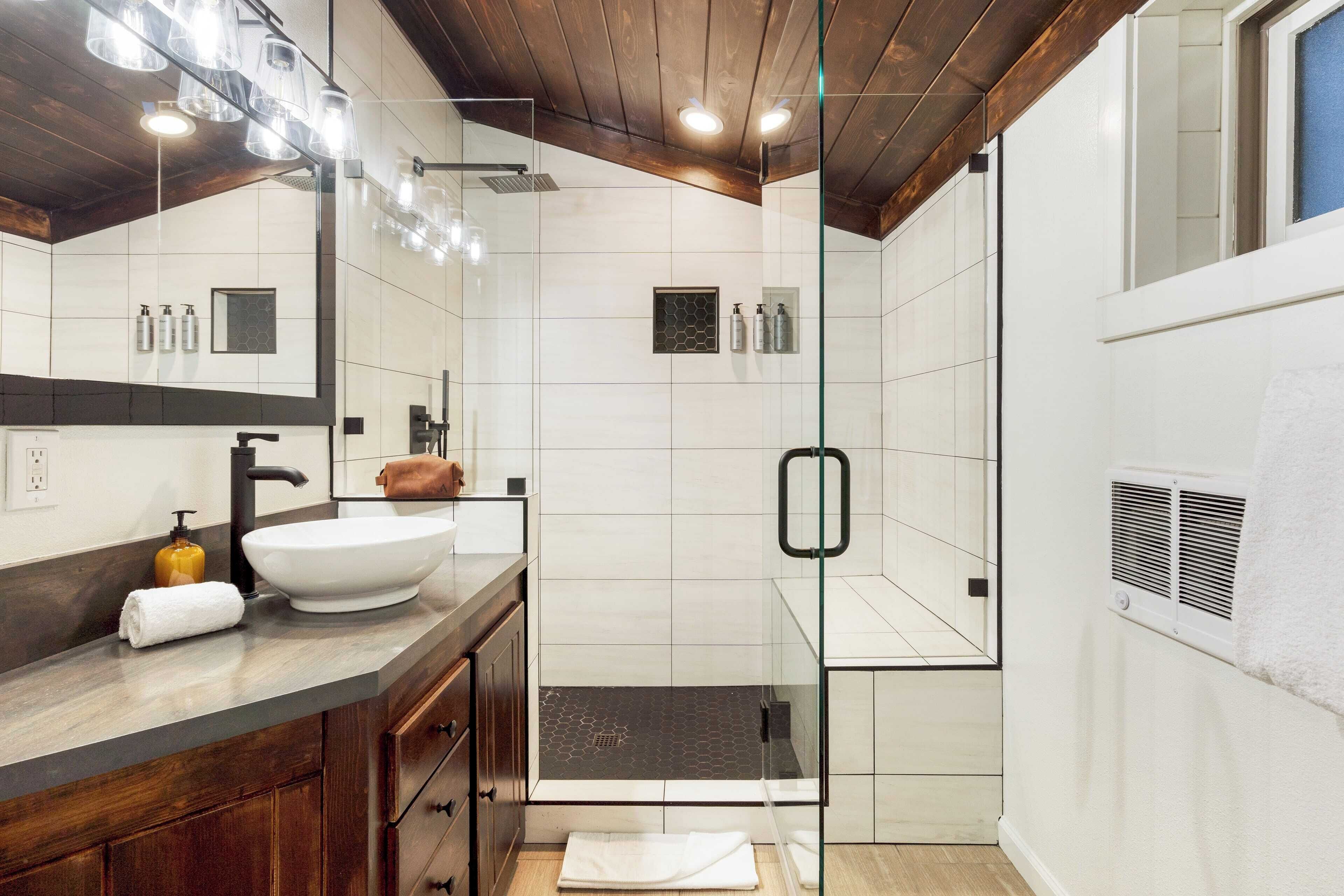 A modern bathroom with a large white sink, dark wooden vanity, glass shower enclosure, and a large mirror.