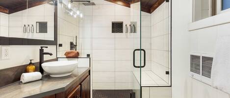 A modern bathroom with a large white sink, dark wooden vanity, glass shower enclosure, and a large mirror.