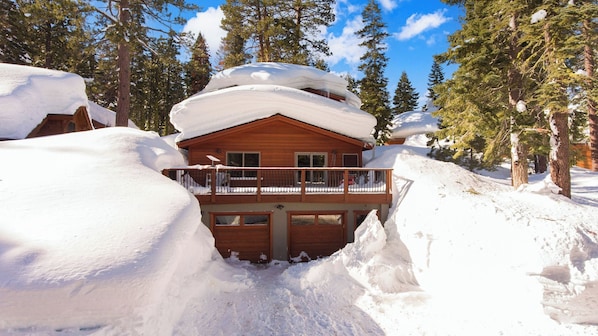 A wooden cabin with a balcony, surrounded by snow-covered trees.