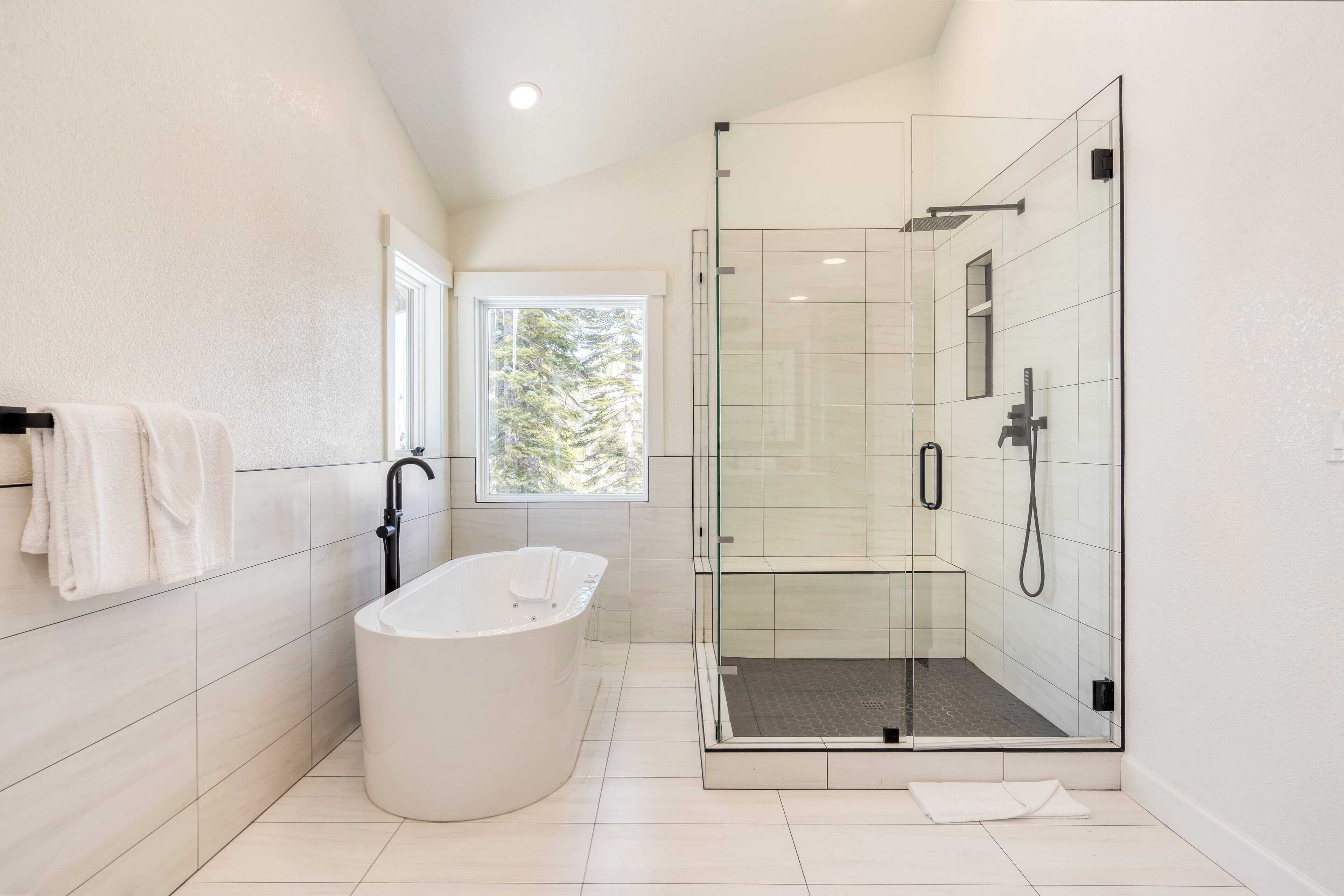 A modern bathroom with a freestanding bathtub, a glass-enclosed shower, and a window providing natural light.