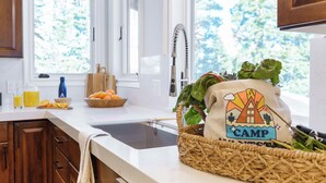 Une cuisine équipée d’un évier, d’une planche à découper, d’un saladier rempli d’oranges, d’une bouteille de jus et d’un panier tressé contenant un sac sur le thème du « camp ».