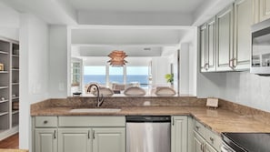 A kitchen with a view of the ocean, a dishwashing area, and a dining area with a view.