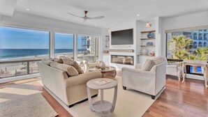 Ein modernes Wohnzimmer mit großem Fenster mit Meerblick, Deckenventilator und flachbildfernseher an der Wand.